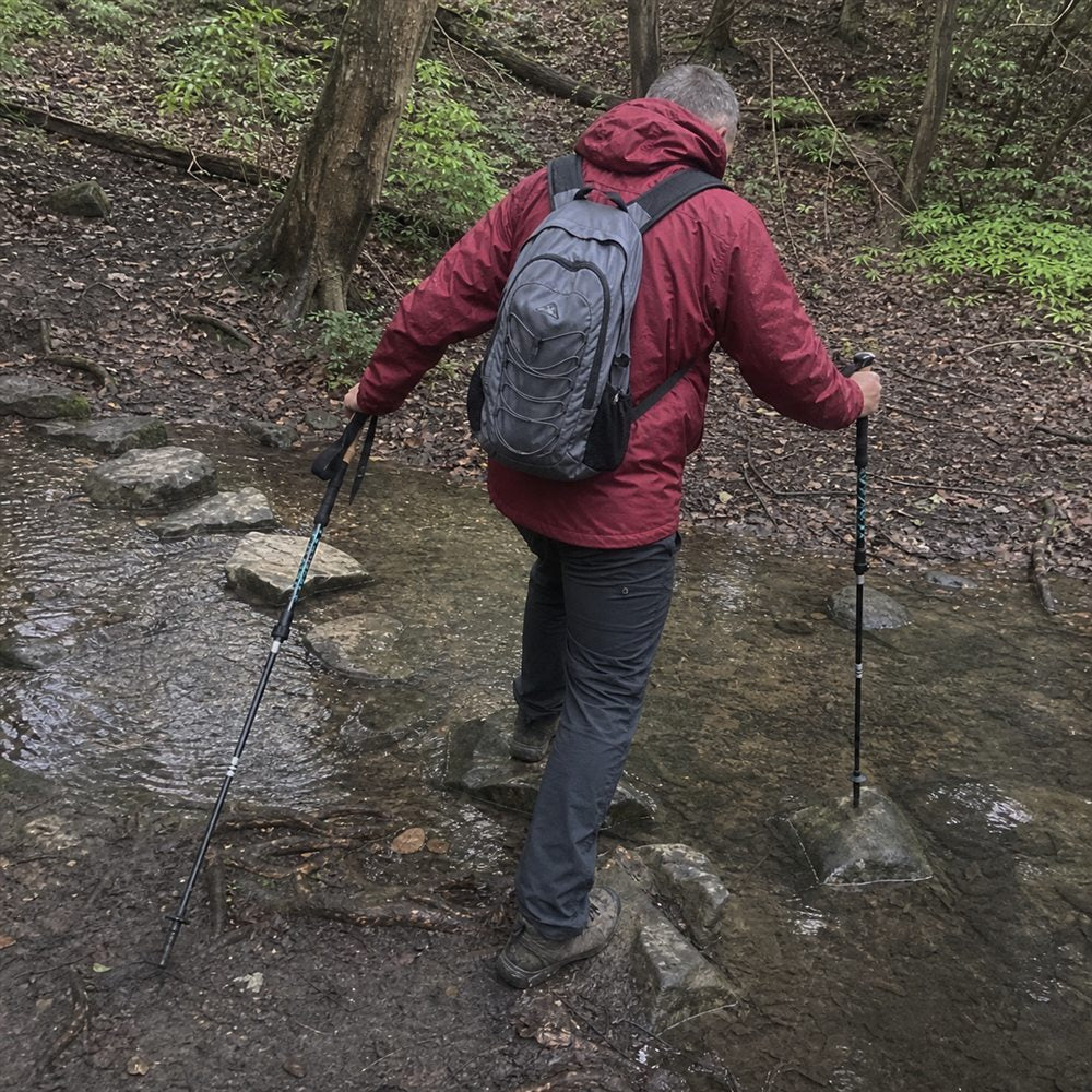 Randonneur utilisant ses bâtons pour traverser un ruisseau rocheux
